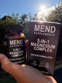 Hand holding the Mend Supplements 5-in-1 Magnesium Complex bottle and box outdoors in sunlight