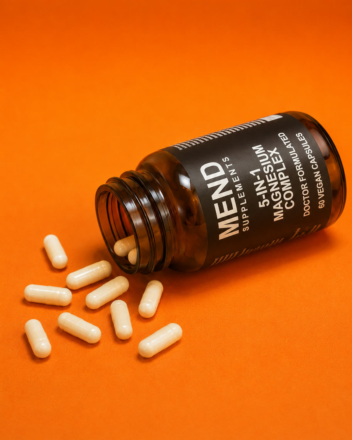 Mend 5-in-1 Magnesium Complex bottle tipped over with capsules spilling onto an orange background